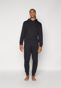 Zwarte hoodie en joggingset gemaakt van zachte stof. De hoodie heeft een trekkoord, terwijl de joggingsbroek elastische cuffs en een elastische tailleband heeft.