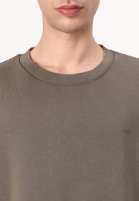 Sweat-shirt en maille vert olive avec un col rond. Présente un logo en relief subtil sur le devant et un tissu doux et texturé.