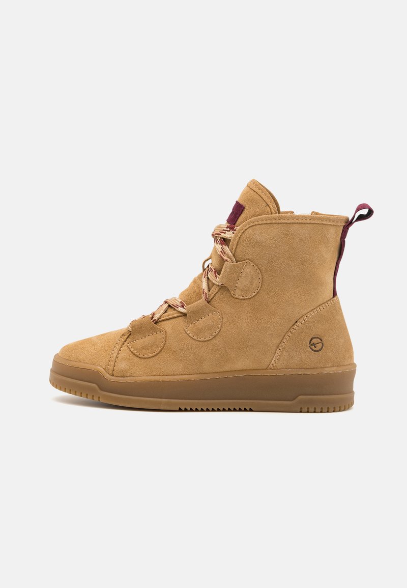Bottines en daim beige avec un col rembourré, bout rond et lacets bordeaux. Présence d'accents ronds et d'une semelle en caoutchouc texturée.