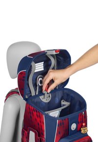 Sac à dos rouge et bleu avec des motifs géométriques, accents gris, rabat supérieur ouvert, montrant les compartiments intérieurs et un porte-clés avec une figurine d'ours.