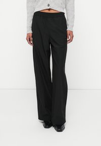 Pantaloni negri, ușori, cu picioare largi și talie elastică. Au un mic logo pe lateral. Textură netedă, cu un design casual.