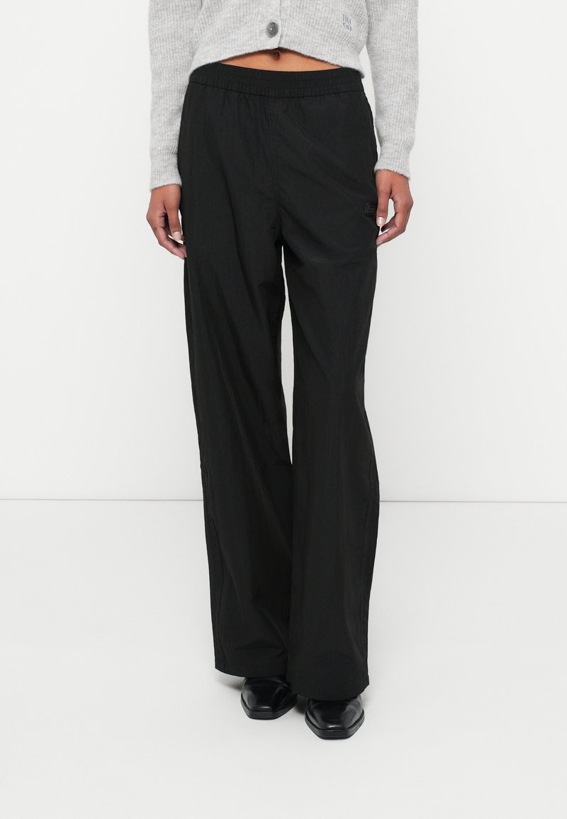 Pantaloni negri, ușori, cu picioare largi și talie elastică. Au un mic logo pe lateral. Textură netedă, cu un design casual.