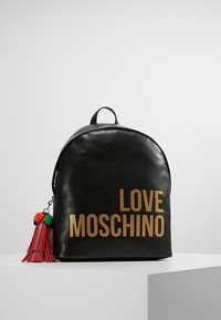 Černý kožený batoh s zlatým textem "LOVE MOSCHINO" a červeným třásňovým přívěskem s barevnými pom-pomy připevněným na zipu.