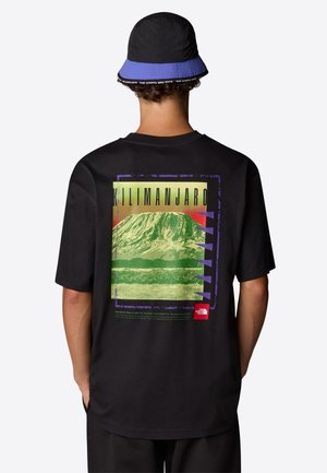 Camiseta de algodón negra con un gráfico de montaña en colores verde y rojo, texto "Kilimanjaro" y un pequeño logotipo rojo en la esquina inferior.