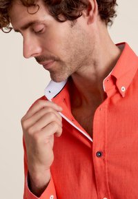 Chemise corail à manches courtes avec un col boutonné, présentant un col intérieur à rayures contrastantes et de subtils accents brodés.