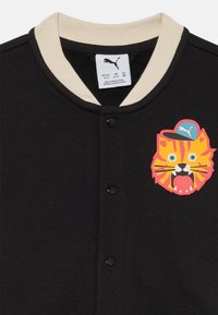 Chaqueta negra con un cuello crema, que presenta un gráfico colorido de cara de tigre y cinco botones negros en la parte delantera.