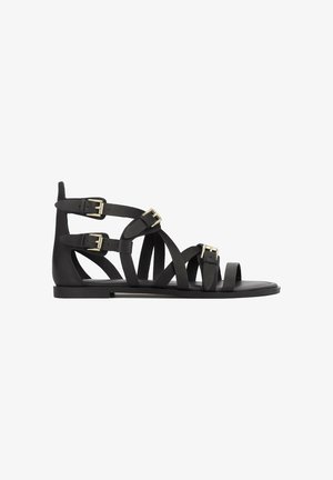 Sandale gladiator negre din piele netedă, cu multiple barete și catarame aurii. Talpă plată și design decupat în vârf.