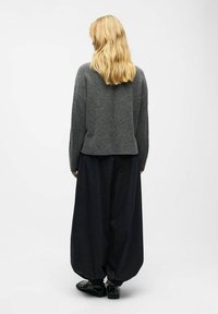 Szary wełniany sweter o luźnym kroju, w po�łączeniu z ciemnymi spodniami typu wide-leg oraz czarnymi butami wsuwanymi. Gładka faktura, minimalistyczny design.
