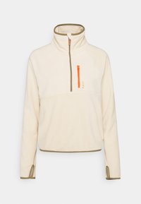 Polarowy pulower w kolorze kremowym z oliwkowymi akcentami. Posiada półsuwnicę z pomarańczowymi detalami, rękawy raglanowe oraz boczne rozcięcia na dolnym brzegu.