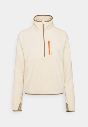 Pull en polaire, couleur crème avec des accents vert olive. Comprend une demi-fermeture éclair avec des détails orange, des manches raglan et des fentes sur les côtés à l'ourlet.