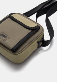 Umhängetasche aus robustem Stoff. Farbblockdesign in Olivgrün und Beige. Verfügt über einen Frontklappenverschluss und einen schwarzen Trageriemen. Kompakte, rechteckige Form.