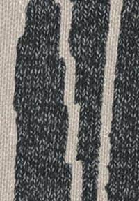 Tissu tricoté beige avec des motifs noirs abstraits, présentant des rayures sombres irrégulières qui créent un aspect texturé.