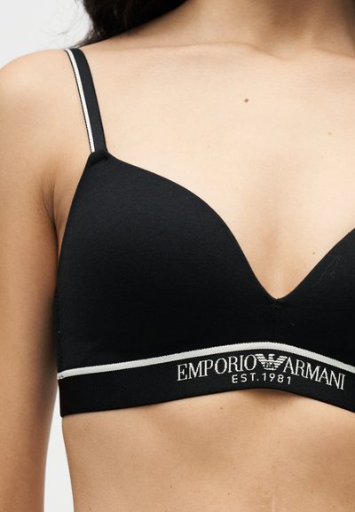 Γυναίκα που φοράει μαύρο σουτιέν Emporio Armani με λευκή επένδυση και λογότυπο στη ζώνη, που δείχνει το πάνω μέρος του στήθους και της περιοχής των ώμων.