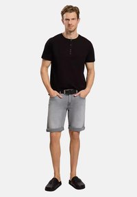 Czarny t-shirt z krótkim rękawem w stylu henley z trzema guzikami, zestawiony z jasnoszarymi szortami dżinsowymi z podwiniętymi mankietami i czarnymi butami wsuwanymi.