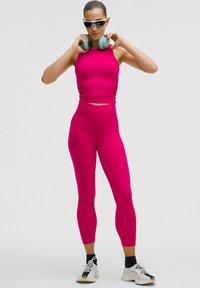 Fuksia crop top dengan tekstur kerut dipadukan dengan legging fuchsia ketat. Dipakai dengan headphone dan kacamata hitam, serta sepatu atletik.