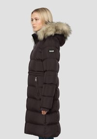 Zwarte gewatteerde jas met capuchon getrimd met bont, horizontale doorgestikte structuur, ritszakken en een getailleerd ontwerp.