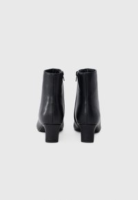 Ζευγάρι μαύρες δερμάτινες μποτάκια μέχρι τον αστράγαλο με χαμηλούς χοντρούς τακούνια και φερμουάρ στην πίσω πλευρά, σε λευκό φόντο.