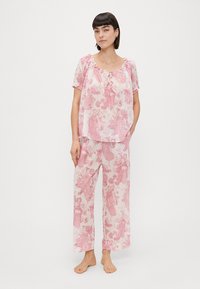 Conjunto de pijama leve e rosa com um padrão floral. A parte de cima tem um decote redondo com um detalhe de laço e mangas curtas; as calças são folgadas.