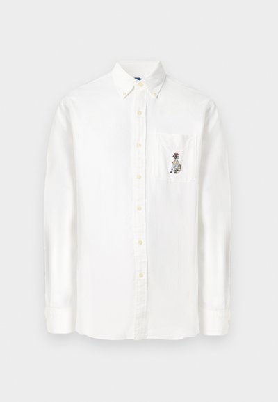 Balta garās piedurknes pogājamā krekls, kas izgatavots no kokvilnas maisījuma, ar krūšu kabatu ar krāsainu izšuvumu, standarta apkakli un noapaļotu apakšmali.