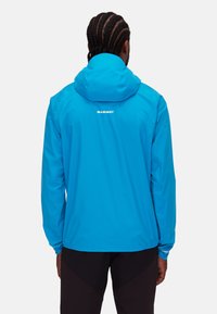 Veste imperméable bleue avec capuche, arborant un logo blanc dans le dos, des poignets élastiques et un tissu lisse et léger.