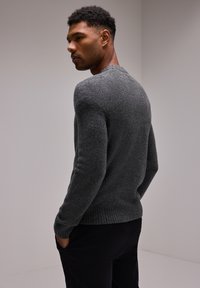 Pull en laine gris avec bord côtelé en bas et aux poignets, design ajusté avec des manches longues. Modèle vu de dos, sur un fond uni.