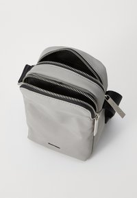 Borsa a tracolla grigia con molteplici scomparti con zip, realizzata in tessuto morbido. Presenta una tracolla nera e dettagli in metallo argentato.