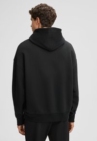 Felpa nera con cappuccio rotondo e grande, realizzata in tessuto morbido, con spalle scese e vestibilità rilassata.