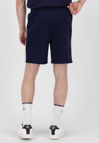 Marineblå treningsshorts med slim fit, med elastisk linning, sidestroppdetaljer og baklomme. Brukt med hvite sokker og joggesko.