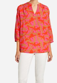 Rode blouse met een V-hals en driekwartmouwen, met een patroon van roze en tan vogel. Gemaakt van lichte, gladde stof.