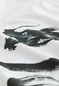 Selymes fehér anyag, absztrakt fekete és türkiz ecsetvonásmintákkal, változó textúrákkal és folyékony alakzatokkal az anyag egészén.