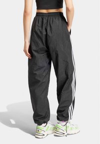 Svarta, lätta träningsbyxor med en texturerad yta, elastisk midja och vita sidostripes. I kombination med vita sneakers med gröna detaljer.