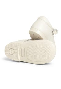 Botas color crema con parte superior de cuero suave, un pequeño detalle de hebilla y una suela de goma texturizada con un patrón de rejilla.
