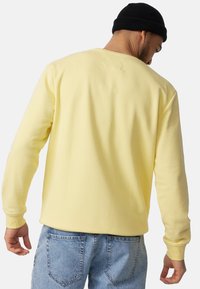 Gul langærmet sweatshirt med ribbede manchetter og rund hals, parret med lyseblå denim jeans. Glat, blød tekstur.
