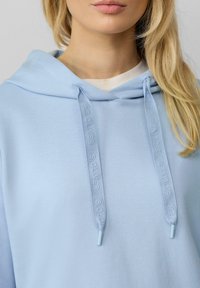 Felpa in cotone azzurro chiaro con cappuccio e cordino, caratterizzata da un marchio testurizzato. Design semplice, texture liscia e tasca a marsupio frontale.