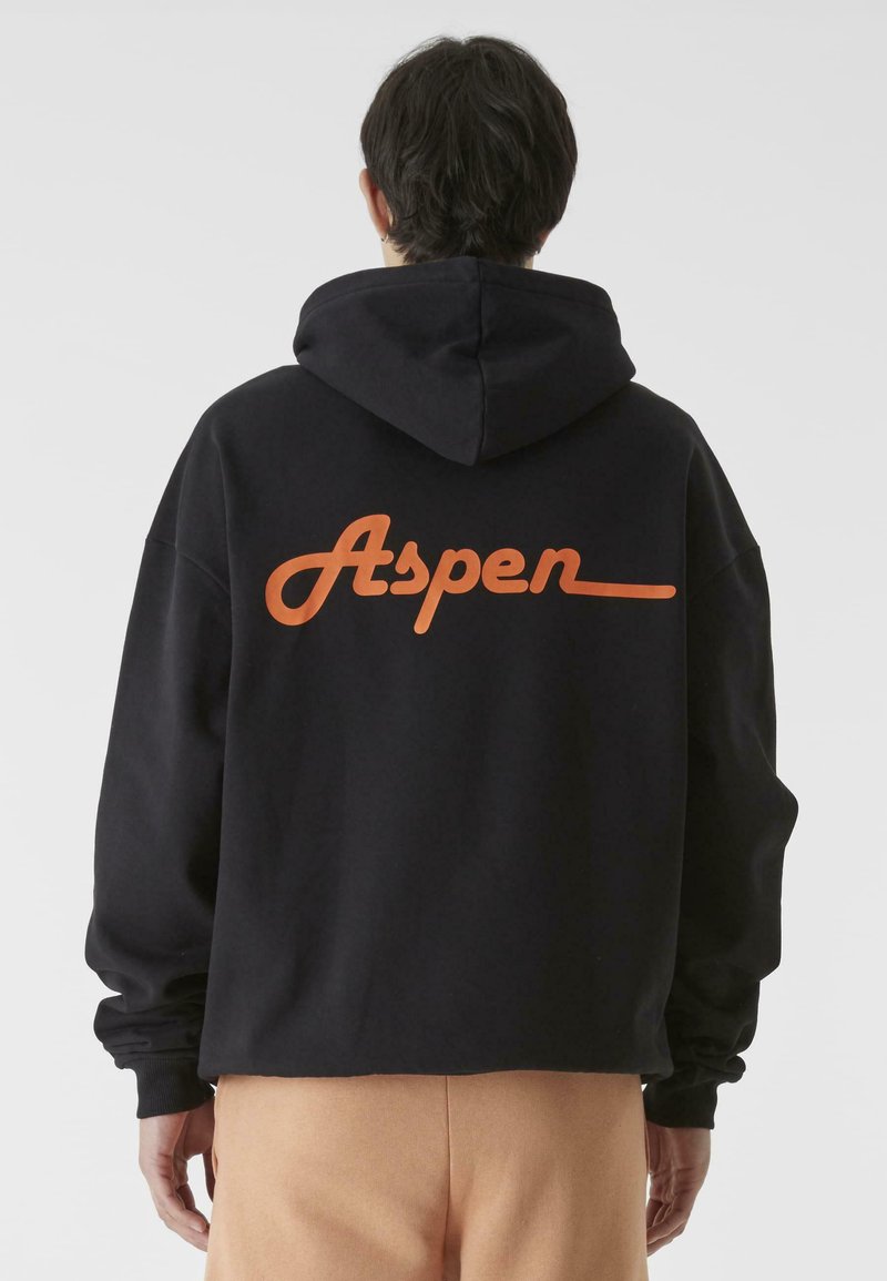 Fekete kapucnis pulóver puha anyagból, amelyen egy hangsúlyos narancssárga "Aspen" logó található a hátsó részen. Nagy méretű fazon, kenguruzsebbel és nagy kapucnival.