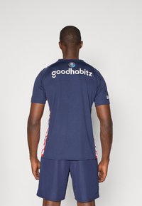Marinblå idrottströja med "goodhabitz"-text på ryggen, röd och vit rutmönstrad siddekor, korta ärmar och matchande marinblå shorts.