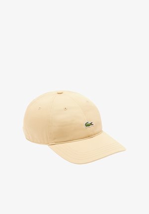 Gorra de béisbol beige con visera curva y logo bordado de cocodrilo verde en el panel frontal.