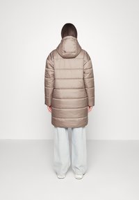 Long beige puffer coat with a hood, featuring a quilted design and a straight hem, paired with wide light denim pants.