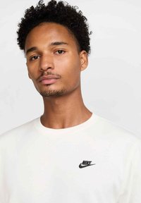 T-shirt bianca a girocollo in cotone, con un piccolo logo Nike nero sul lato sinistro del petto. Design semplice con maniche corte.