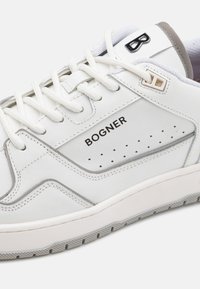 White leather sneaker with grey accents, rounded toe, perforated side detailing, flat white laces, and rubber sole. "BOGNER" logo visible.