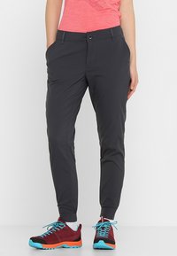 Osoba oblečená v tmavých úzkých kalhotách, korálovém tričku, bílých ponožkách a burgundských sportovních botách s jasně modrými tkaničkami a oranžovými podrážkami.