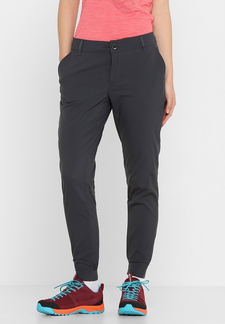 Osoba oblečená v tmavých úzkých kalhotách, korálovém tričku, bílých ponožkách a burgundských sportovních botách s jasně modrými tkaničkami a oranžovými podrážkami.