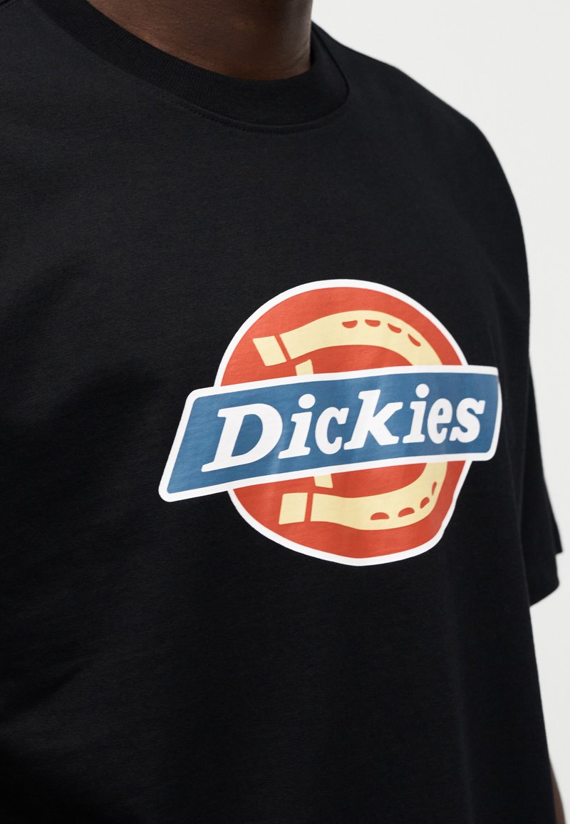 Maglietta nera in cotone con grafica circolare in rosso, blu e giallo, con la scritta "Dickies" e un design a ferro di cavallo.
