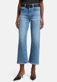 Ljusblå vida denimjeans med kontrastsömmar, medelhögt midja och unik fickdesign, parat med ett svart texturerat bälte.