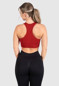 Sujetador deportivo rojo con diseño de espalda de corredor. Presenta una forma ajustada y una tela texturizada. Combinado con leggings negros de tiro alto.