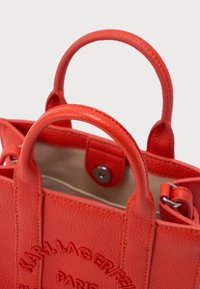 Piros, texturált bőrtáska dupla fogantyúval és mágneses kapoccsal, a KARL LAGERFELD PARIS márkanevének domború nyomtatásával.