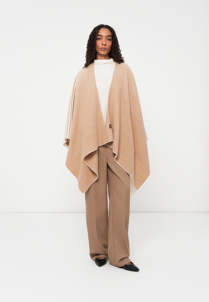 Beiger Wollponcho mit strukturiertem Design, der eine drapierte Silhouette, asymmetrische Kanten und ein dezentes Streifenmuster aufweist.