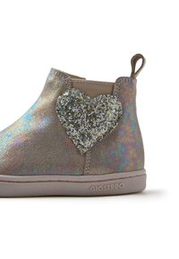 Stivaletto metallizzato e iridescente in beige con un dettaglio a forma di cuore in glitter argento testurizzato sul lato. Suola in gomma e linguetta sul retro.