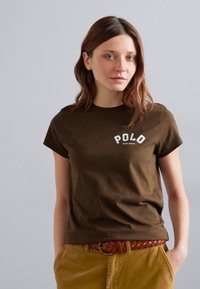 Brązowa bawełniana koszulka z krótkim rękawem, z białym logo "POLO" na klatce piersiowej. W połączeniu z żółtymi spodniami z korduroju o teksturowanej powierzchni.