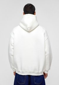 Witte oversized hoodie met een grote capuchon, verlaagde schouders en geribbelde manchetten. Zachte textuur en een schoon, minimalistisch ontwerp.